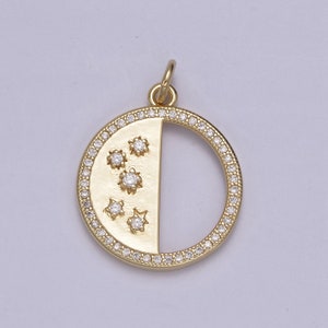 May include: Gold-tone pendant with a half-moon design. The pendant features a circle of small, clear stones around the outer edge. The other half of the circle has a flat surface with five star-shaped clear stones. A small loop is at the top.