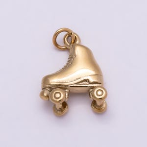 May include: A polished gold-tone metal charm shaped like a classic roller skate. The charm features a high-top boot design with visible laces, a defined heel, and four small wheels attached to the base. A circular jump ring is attached at the top.