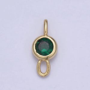 K&ouml;nnte beinhalten: Goldfarbener Anh&auml;nger mit einem gr&uuml;nen Edelstein und einer Schlaufe zum Anbringen an einer Kette oder einem Armband.