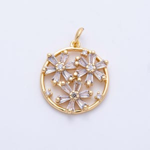 May include: A gold-colored pendant with a circular design. The pendant features three flower-shaped arrangements with clear, rectangular-cut stones and a central round stone. Small, round stones are scattered around the flowers.