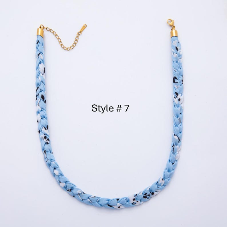 May include: A braided necklace in light blue fabric with a pattern of white and black shapes. The necklace has gold-colored metal clasps and chain. The text "Style # 7" is printed on the image.