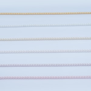 May include: Close-up of several strands of delicate pearl necklaces in various colors, including gold, white, and pink. The pearls are small and evenly spaced, creating a refined and elegant aesthetic. The necklaces are displayed against a plain white background.