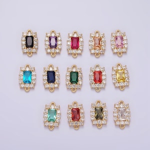 Könnte beinhalten: Zwölf goldfarbene rechteckige Verbindungsanhänger mit einem klaren Kristallrand und einem farbigen Edelstein in der Mitte. Die Edelsteine sind schwarz, lila, rot, orange, rosa, blau, dunkelblau, grün, rot, gelb, grün und braun.