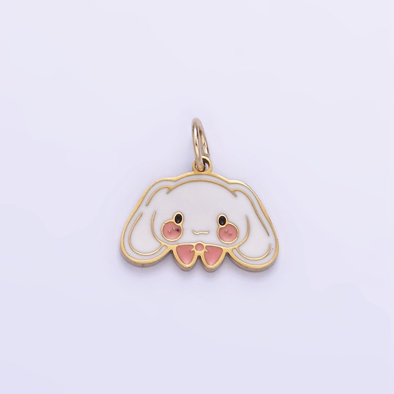 Op de afbeelding: Een gouden hanger met een wit konijnengezicht en roze wangen. Het konijn draagt een roze strik.