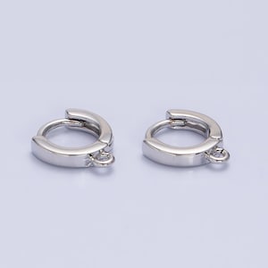 Puede incluir: Un par de pendientes de aro de plata con un pequeño bucle a cada lado. Los aros son planos y tienen un acabado liso.