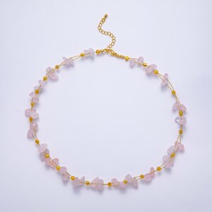 May include: A delicate necklace featuring small, irregular pink rose quartz stones strung on a gold-colored wire. The necklace has a gold-colored chain and small gold beads interspersed between the stones. The necklace is displayed on a white background.