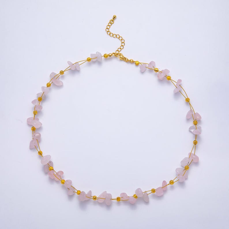May include: A delicate necklace featuring small, irregular pink rose quartz stones strung on a gold-colored wire. The necklace has a gold-colored chain and small gold beads interspersed between the stones. The necklace is displayed on a white background.