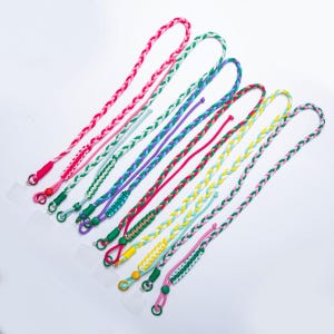 Könnte beinhalten: Eine Sammlung farbenfroher geflochtener Schlüsselbänder in verschiedenen Farbtönen, darunter Rosa, Grün, Lila und Gelb. Jedes Schlüsselband hat einen kleinen Metallring und ein klares Kunststoffteil. Die Schlüsselbänder sind für ein Telefon oder andere kleine Gegenstände konzipiert.