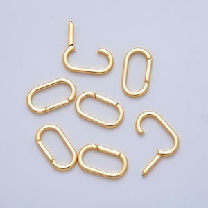 May include: A collection of gold-colored oval carabiner clasps. The clasps are in various positions, some closed and some open, showcasing their functionality. The smooth, metallic finish reflects light, highlighting their shape and design. These clasps are suitable for jewelry making or crafting.