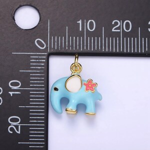 May include: A gold-colored charm in the shape of a blue elephant with a white ear and a pink flower on its back.