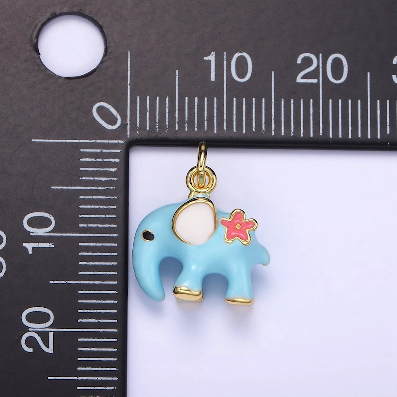 May include: A gold-colored charm in the shape of a blue elephant with a white ear and a pink flower on its back.