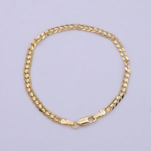 May include: A gold-colored bracelet with a curb chain design. The bracelet features a series of interlocking links, creating a flat, textured surface. A lobster clasp secures the bracelet. The jewelry is displayed against a plain background.