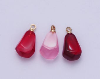 Puede incluir: Tres colgantes de cristal en rojo, rosa y rojo oscuro. Cada colgante tiene un bucle dorado en la parte superior.