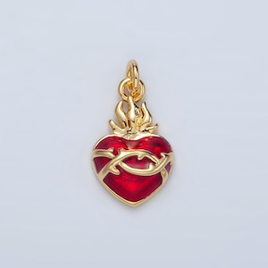 May include: A gold-colored pendant featuring a red heart design with a gold-colored thorn crown. The heart is surrounded by gold flames. The pendant is designed to be worn as a necklace.