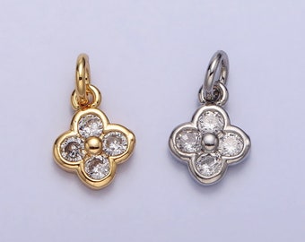 May include: Two clover-shaped pendants. One is gold-toned, the other silver-toned. Each pendant features four clear, round gemstones surrounding a central gemstone. The pendants have a small loop at the top for attaching to a chain or bracelet.