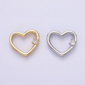 May include: Two heart-shaped charms with a single clear rhinestone in the center of each. The charm on the left is gold and the charm on the right is silver.