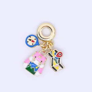 May include: A gold-toned charm with a compass, backpack, and map pendant. The backpack is pink, white, and blue. The map pendant has red, yellow, green, and black accents. The compass is blue with a red needle.