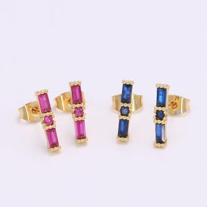 May include: A pair of gold stud earrings with a bar design. One pair features pink cubic zirconia stones and the other pair features blue cubic zirconia stones.