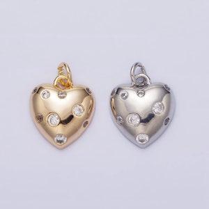 May include: Two heart-shaped pendants with a dotted design. One pendant is gold with clear stones, the other is silver with clear stones.