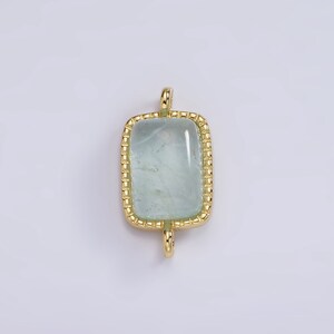 May include: A gold-toned pendant with a light blue rectangular gemstone set in a gold frame. The pendant has a loop at the top for attaching to a chain.