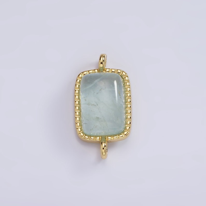 May include: A gold-toned pendant with a light blue rectangular gemstone set in a gold frame. The pendant has a loop at the top for attaching to a chain.