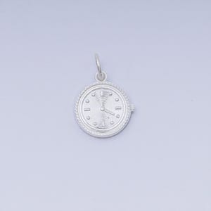 May include: A silver-colored charm in the shape of a watch. The watch face has a circular design with small dots marking the hours and two hands indicating the time. The charm has a loop at the top for attaching to a necklace or bracelet.