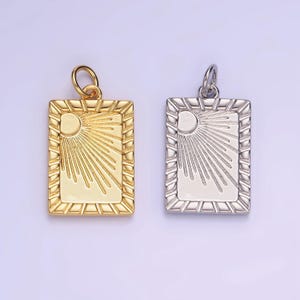 May include: Two gold and silver pendants with a sunburst design. The pendants are rectangular with a textured border and a raised sunburst design in the center.