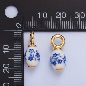 May include: Two gold-toned charms with blue and white porcelain egg-shaped beads. Each bead has a floral design. The charms are approximately 1 inch in length.
