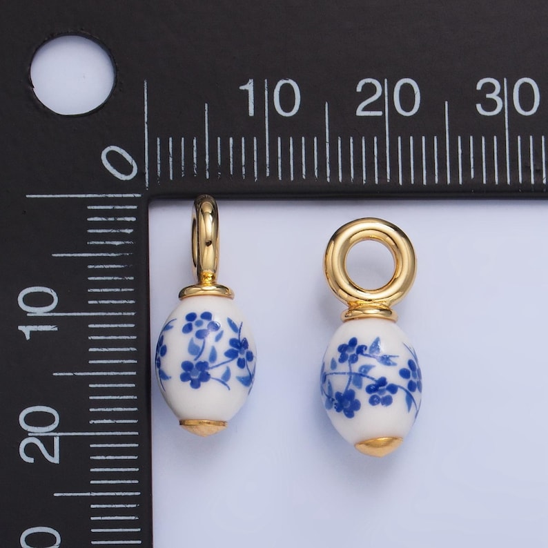 May include: Two gold-toned charms with blue and white porcelain egg-shaped beads. Each bead has a floral design. The charms are approximately 1 inch in length.