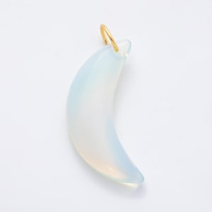 Op de afbeelding: Een maanvormige hanger met een goudkleurige lus. De hanger heeft een bleke, doorschijnende blauw-witte kleur. De maanvorm is glad en gebogen, met een subtiele kleurovergang.