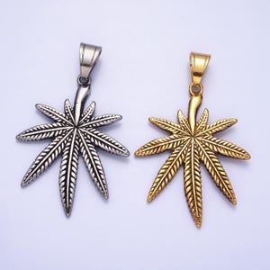 May include: Two silver and gold marijuana leaf pendants. The pendants are detailed with intricate leaf veins and have a bail for attaching to a chain.