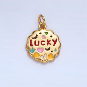 May include: Gold charm with a round, cookie-shaped design. The charm is decorated with colorful enamel and the word "LUCKY" in red.