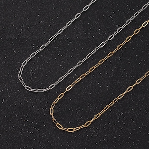 May include: Two chain necklaces, one silver and one gold, on a black background. Both necklaces are made of small, linked oval shapes.
