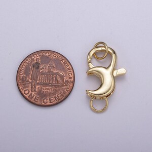 May include: Gold-toned metal lobster clasp with a crescent moon design. The clasp is about the size of a US penny.