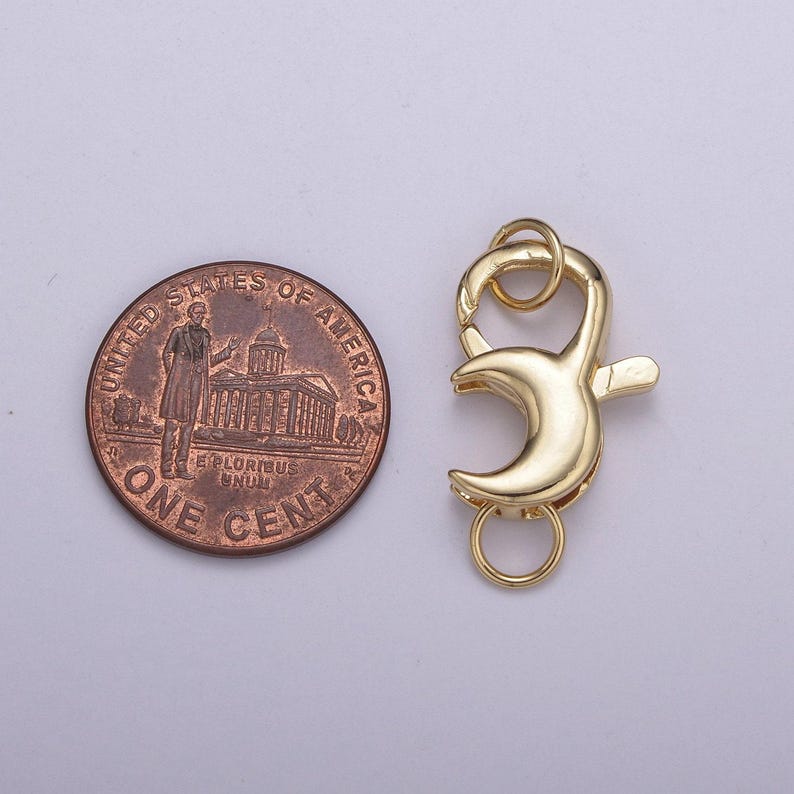 May include: Gold-toned metal lobster clasp with a crescent moon design. The clasp is about the size of a US penny.