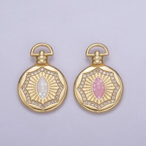 May include: Two gold-toned pendant charms with a round shape and a decorative design. Each charm features a white or pink oval-shaped stone in the center.