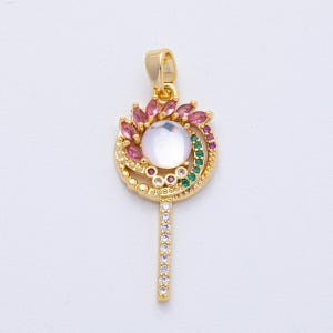 May include: Gold-toned pendant with a lollipop design. The pendant features a large, round, iridescent stone at the center, surrounded by pink and green gemstones. The stem is adorned with clear crystals.