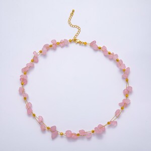 May include: A delicate necklace featuring small, irregular pink gemstones strung on gold-colored wire. The necklace has a gold-colored chain and clasp. The gemstones are a soft pink color.