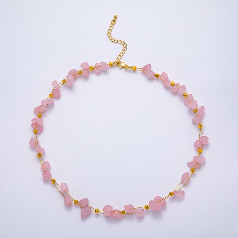 May include: A delicate necklace featuring small, irregular pink gemstones strung on gold-colored wire. The necklace has a gold-colored chain and clasp. The gemstones are a soft pink color.