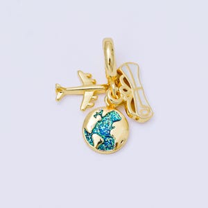 May include: A gold-colored travel-themed charm with a small airplane, a globe with blue and green glitter, and a scroll. The charm is designed to be attached to a bracelet or necklace.