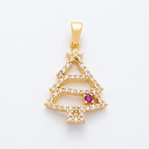 May include: A gold-colored Christmas tree pendant with a star on top. The tree is encrusted with clear, round gemstones and a single red gemstone. The pendant has a loop for a chain.