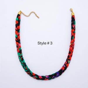 May include: Braided necklace with a mix of red, green, pink, and black fabric. The necklace has gold-colored metal clasps and a chain for adjusting the length. The text "Style # 3" is visible.