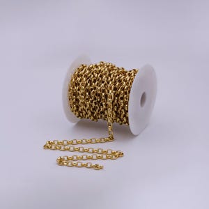 May include: A spool of gold-colored chain, with a portion of the chain uncoiled and lying on a white surface.