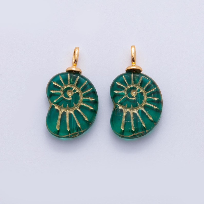 May include: Two green glass pendant charms with a spiral design in gold. Each charm has a gold-colored loop at the top for hanging. The charms are a sea green color and are set against a white background.