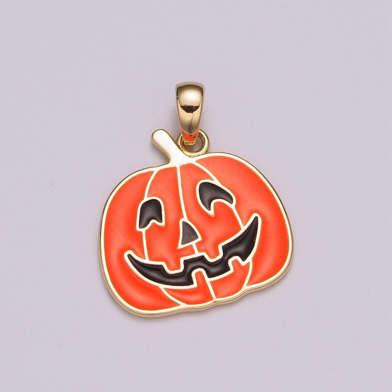 Pu&ograve; includere: Un ciondolo dorato a forma di zucca di Halloween con un viso sorridente nero. La zucca &egrave; arancione con occhi, naso e bocca neri.
