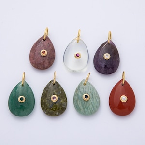 May include: Seven teardrop-shaped pendants in various colors, including red, green, and purple. Each pendant features a gold bail and a small, contrasting gemstone set in a gold bezel. The pendants are displayed against a white background.