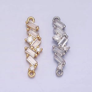 May include: Two decorative jewelry pieces. One is gold-toned, the other silver-toned. Each features a zig-zag pattern of clear rectangular and round-cut crystals. Both have a small loop at the top and bottom for attachment.