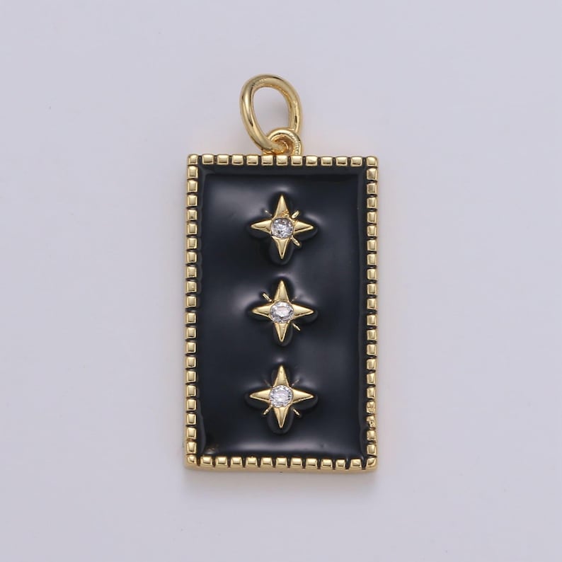 May include: A gold pendant with a black enamel rectangle featuring three gold stars with clear rhinestones. The pendant has a gold bail for attaching to a chain.