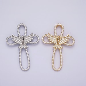 May include: Two silver and gold cross pendants with butterfly designs. Both pendants are encrusted with clear cubic zirconia stones.
