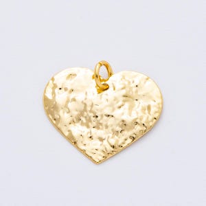 May include: A gold-colored heart-shaped pendant with a hammered texture. The pendant has a small loop at the top for attaching to a chain or other jewelry. The heart is a solid, shiny gold color.